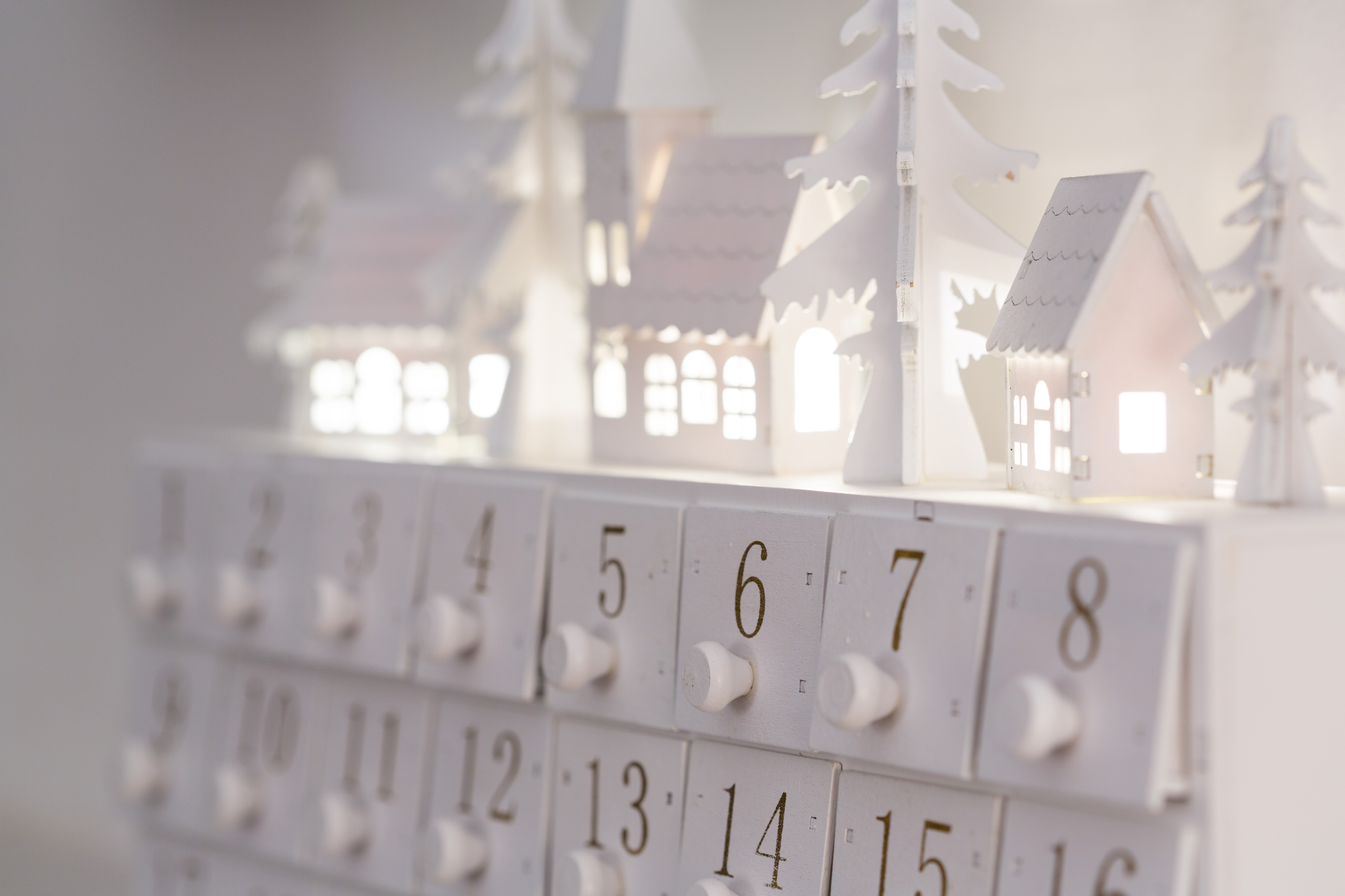 Weisser Adventskalender, im Hintergrund sind beleuchtete Miniaturhäuser zu sehen